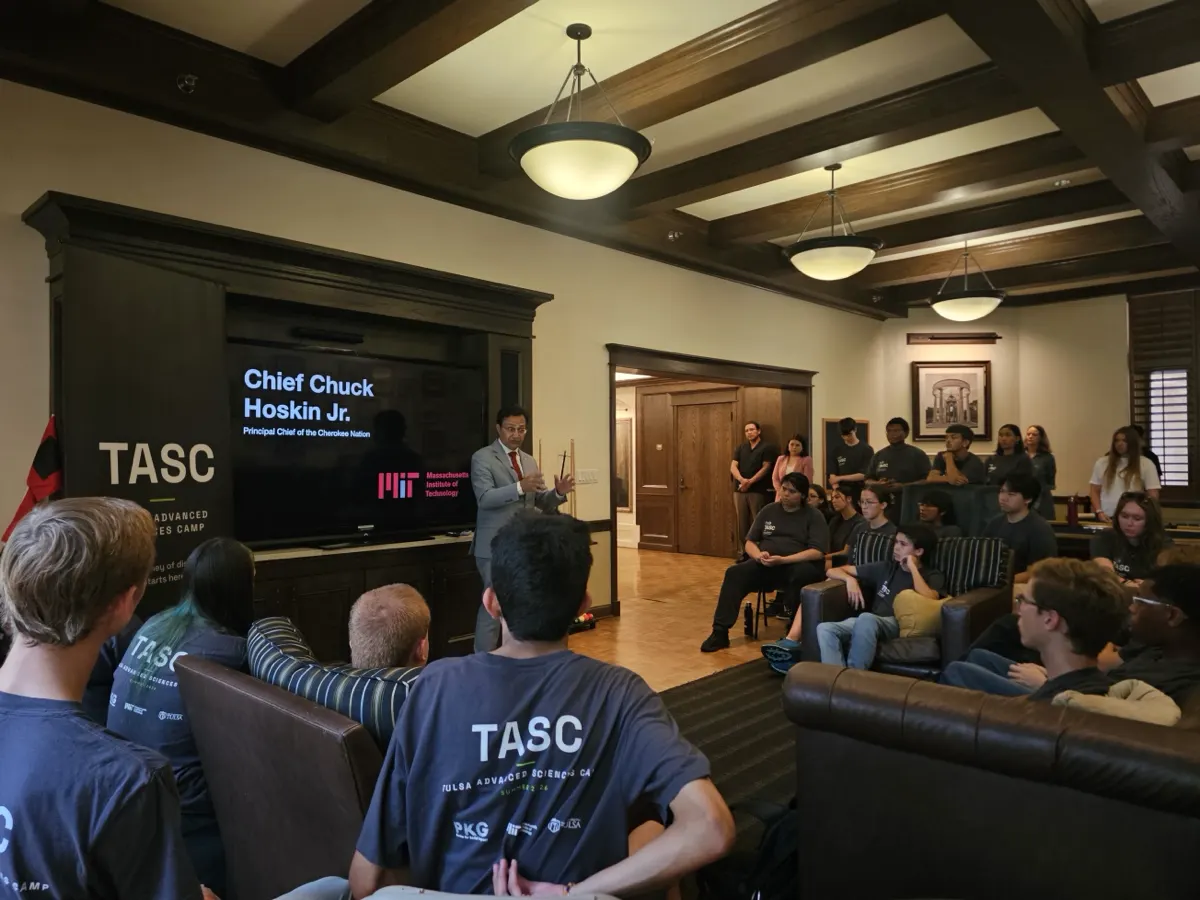 Principal Chief Chuck Hoskin Jr. of the Cherokee Nation speaking to TASC students seated on sofas in a wood-panelled room at the University of Tulsa.